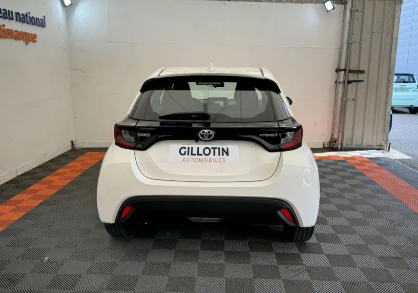 Vue arrière d'une Toyota Yaris hybride blanche 2022 avec bande noire distinctive sur le hayon et feux arrière LED.