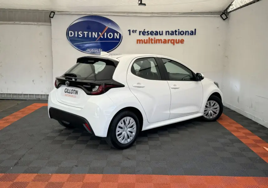 Toyota Yaris hybride blanche vue 3/4 arrière droit en intérieur, avec toit noir et jantes standard.