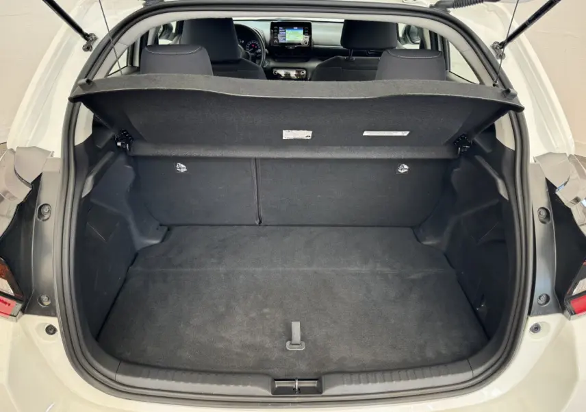 Coffre ouvert d'une Toyota Yaris hybride blanche 2022, vue arrière montrant l'intérieur spacieux et la tablette de coffre relevée.