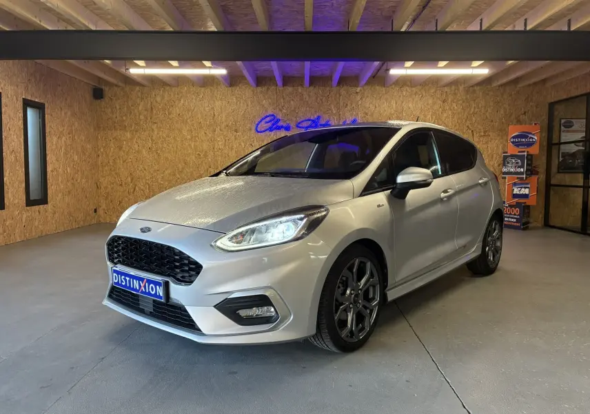 Ford Fiesta 1.0 EcoBoost 95 ST Line gris vue 3/4 avant droit dans un showroom avec éclairage intérieur.