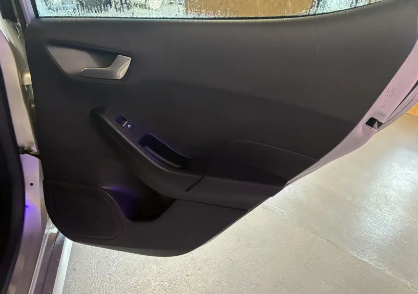 Vue intérieure de la porte arrière gauche grise d'une Ford Fiesta 1.0 EcoBoost 95 ST Line avec commande de fenêtre électrique.