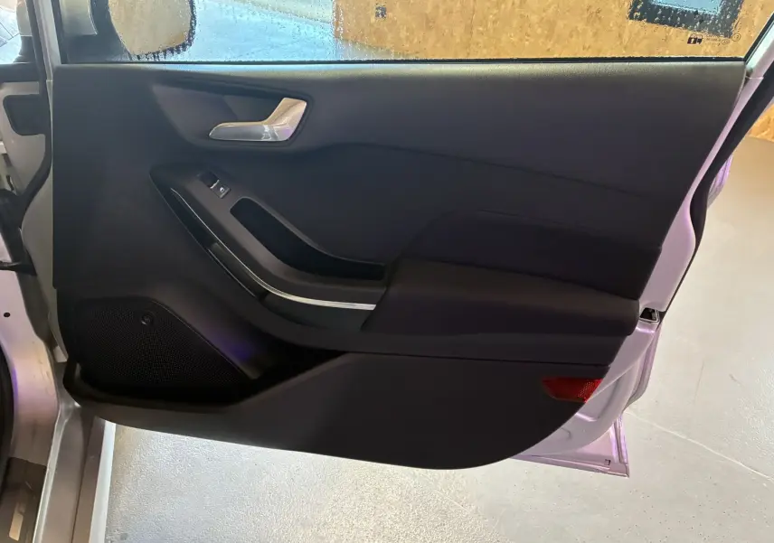 Porte avant gauche ouverte d'une Ford Fiesta gris 2020, intérieur tissu gris-noir avec poignée argentée et haut-parleur intégré.