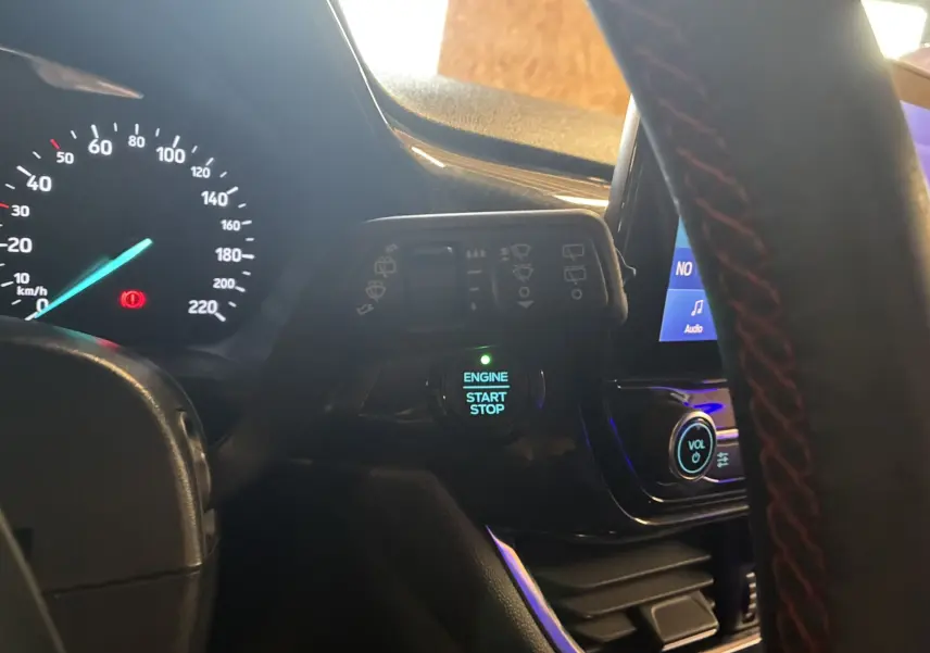 Vue intérieure du tableau de bord d'une Ford Fiesta gris, avec bouton start/stop et commandes au volant visibles.