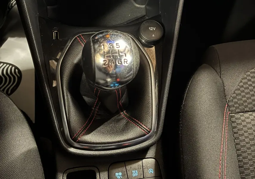 Gros plan sur le levier de vitesses manuel noir avec surpiqûres rouges dans une Ford Fiesta gris 2020, intérieur tissu noir.
