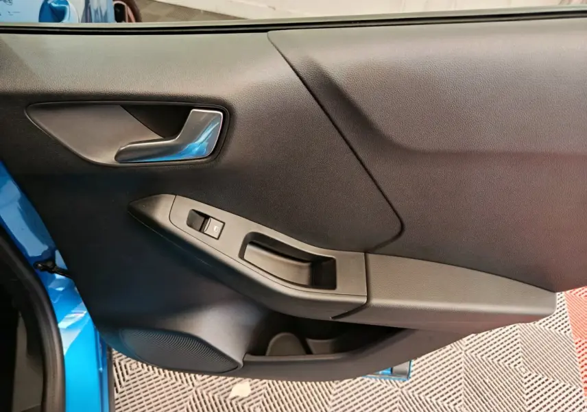 Vue rapprochée de la porte côté gauche du Ford Puma bleu 2025, avec poignée argentée et commande de vitre noire.