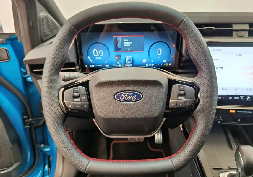 Vue intérieure centrée sur le volant cuir noir à surpiqûres rouges du Ford Puma bleu, avec tableau de bord numérique et écran tactile.