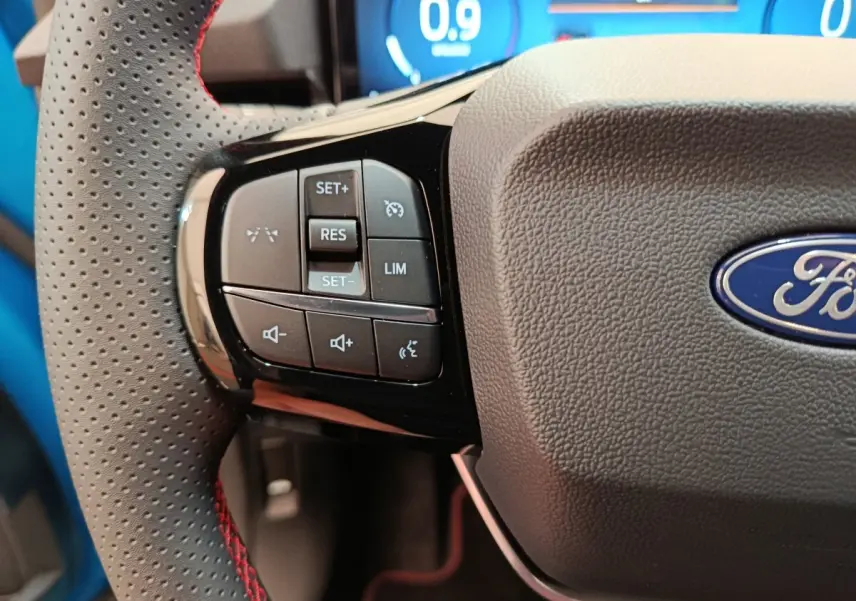 Gros plan sur le volant perforé avec commandes multifonctions du Ford Puma bleu 2025, affichage numérique en arrière-plan.
