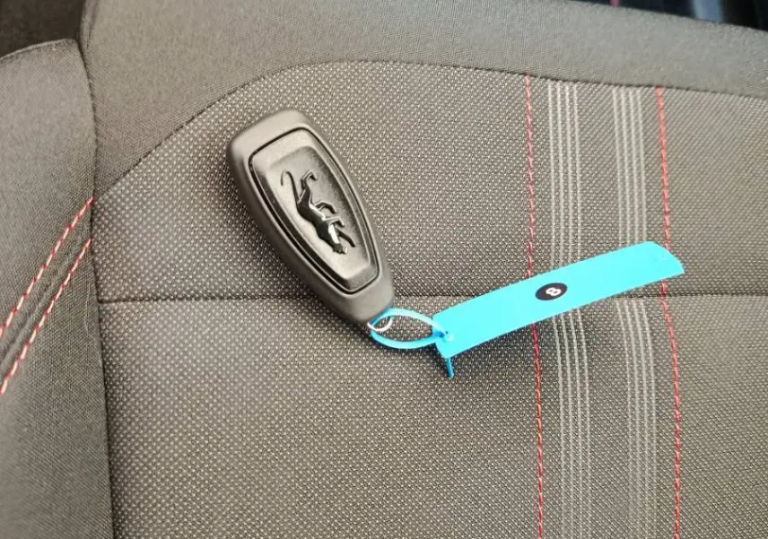 Gros plan sur une clé Ford posée sur un siège tissu gris foncé avec surpiqûres rouges, intérieur du Ford Puma.