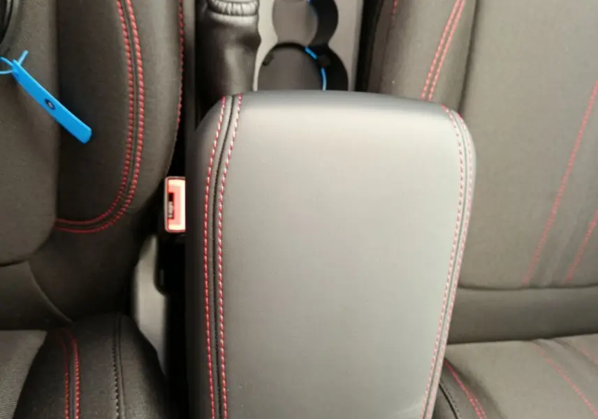 Vue plongeante sur l'accoudoir central noir avec surpiqûres rouges entre les sièges avant du Ford Puma bleu.