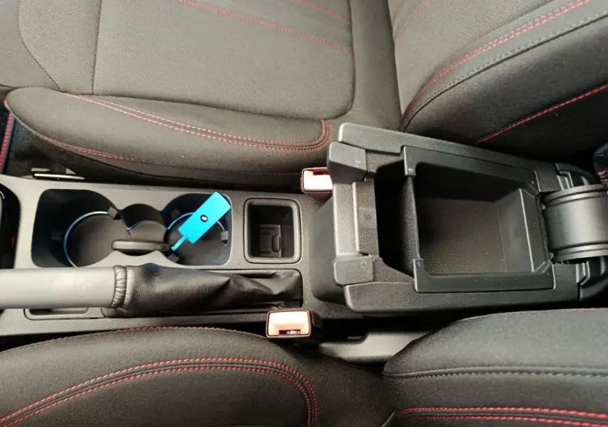 Vue rapprochée de la console centrale du Ford Puma 2025, montrant les sièges noirs avec surpiqûres rouges et un rangement ouvert.