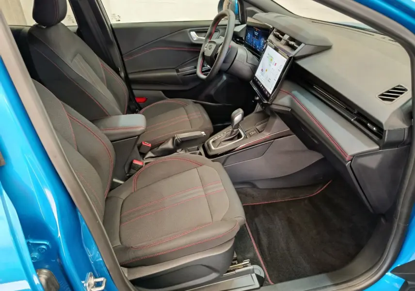 Intérieur avant droit du Ford Puma bleu 2025, sièges noirs avec surpiqûres rouges et écran tactile central visible.