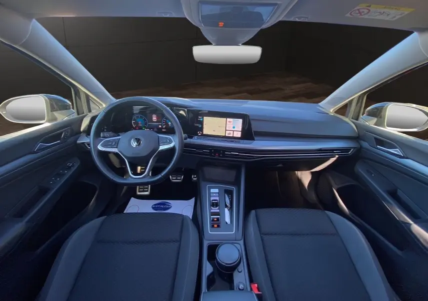 Vue intérieure avant de la Volkswagen Golf VIII noire, tableau de bord numérique et volant multifonction cuir visible.