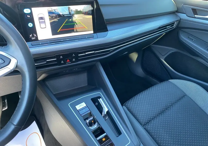 Vue intérieure côté passager de la Volkswagen Golf VIII noire, avec écran tactile affichant la caméra de recul.