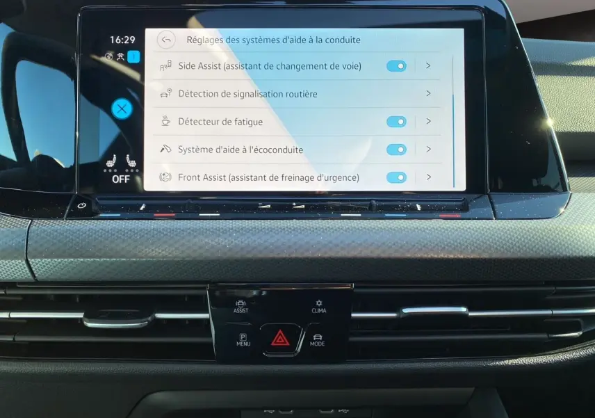 Vue rapprochée de l'écran tactile central de la Volkswagen Golf VIII noire, affichant les réglages d'aide à la conduite.