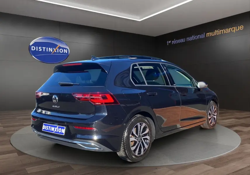 Vue 3/4 arrière droite d'une Volkswagen Golf VIII noire nacrée avec jantes alu et toit panoramique en showroom.