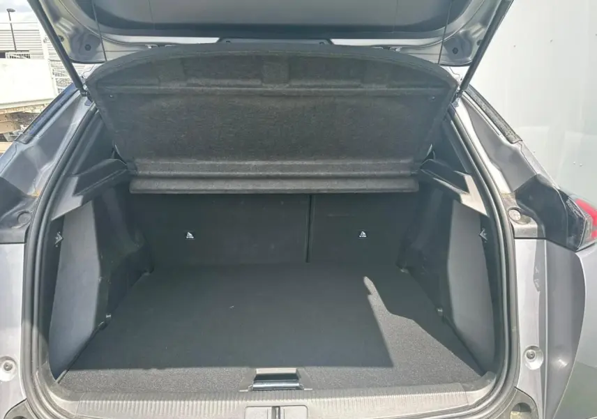 Coffre ouvert d'un Peugeot 2008 gris clair vu de l'arrière, montrant l'espace de chargement vide et la tablette cache-bagages relevée.