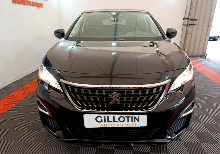 Vue frontale d'un Peugeot 3008 noir 2019 avec calandre chromée et phares allumés en intérieur showroom.
