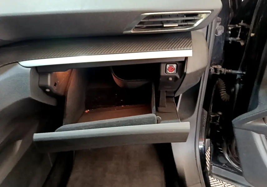 Intérieur du Peugeot 3008 noir, vue côté passager avec boîte à gants ouverte et tableau de bord en carbone.