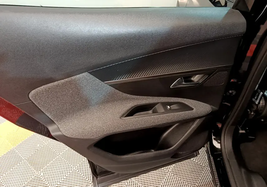 Gros plan sur la porte côté gauche du Peugeot 3008 noir, mettant en valeur les matériaux texturés et la poignée intérieure.
