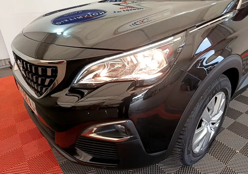 Vue 3/4 avant droit du Peugeot 3008 noir avec phares allumés et jante alliage visible.