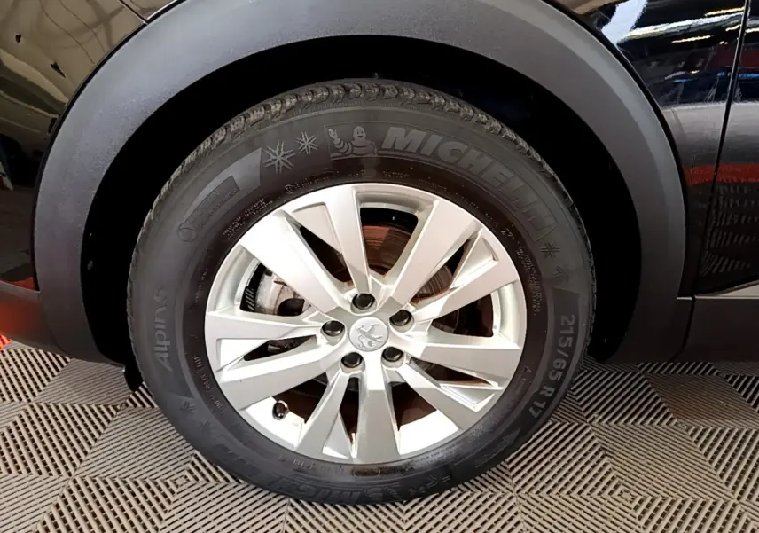 Gros plan sur la roue avant gauche d’un Peugeot 3008 noir, mettant en valeur la jante alliage et le pneu Michelin hiver.