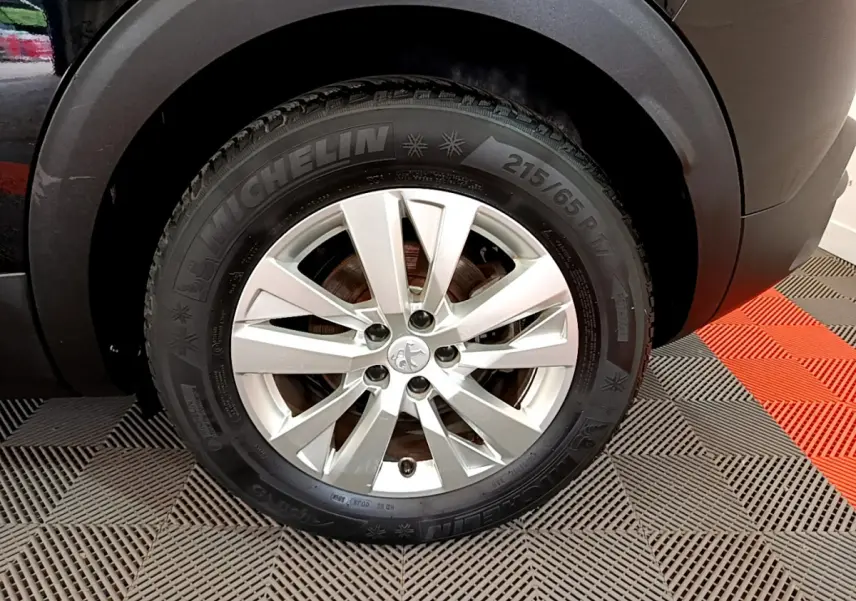 Gros plan sur la roue avant droite d’un Peugeot 3008 noir, jante alliage argentée et pneu Michelin visible.
