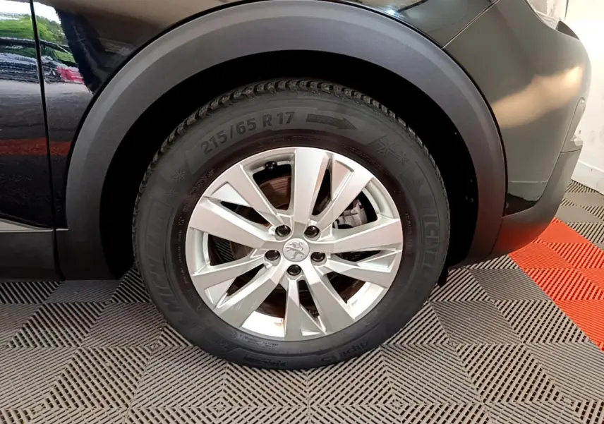 Gros plan sur la roue avant droite noire d’un Peugeot 3008 2019 avec jante argentée et logo lion central.