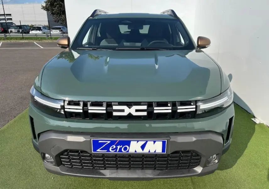 Vue frontale du Dacia Duster III hybride en kaki dusty avec calandre noire et logo central lumineux.