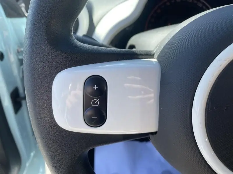 Gros plan sur les commandes de régulateur de vitesse sur le volant noir et blanc d’une Renault Twingo III bleu dragée.