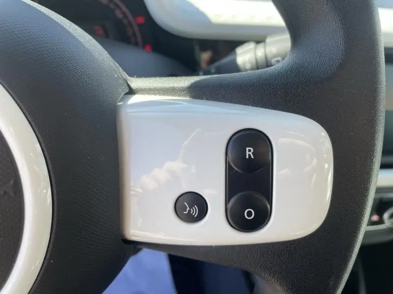 Gros plan sur les commandes blanches et noires du volant de la Renault Twingo III bleu dragée, version 2022.