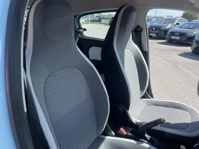 Vue intérieure des sièges avant gris clair et foncé du Renault Twingo III bleu dragée, avec frein à main visible côté droit.