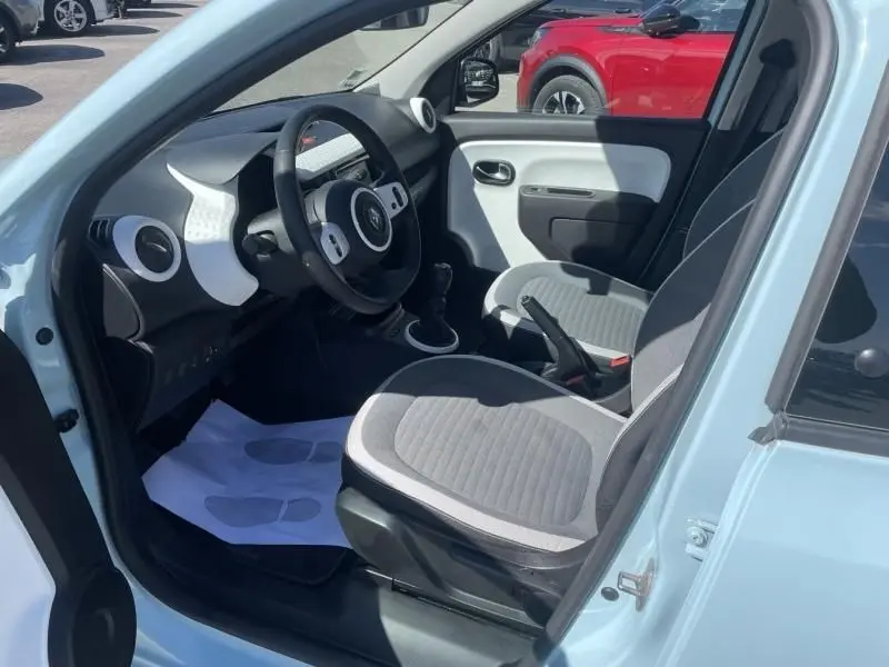 Intérieur avant droit de la Renault Twingo III bleu dragée 2022, volant, sièges gris et levier de vitesse manuel visibles.