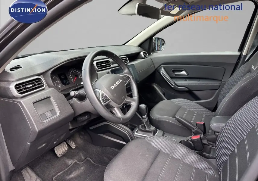 Vue intérieure côté conducteur du Dacia Duster 2024 noir, montrant le tableau de bord et les sièges en tissu noir.