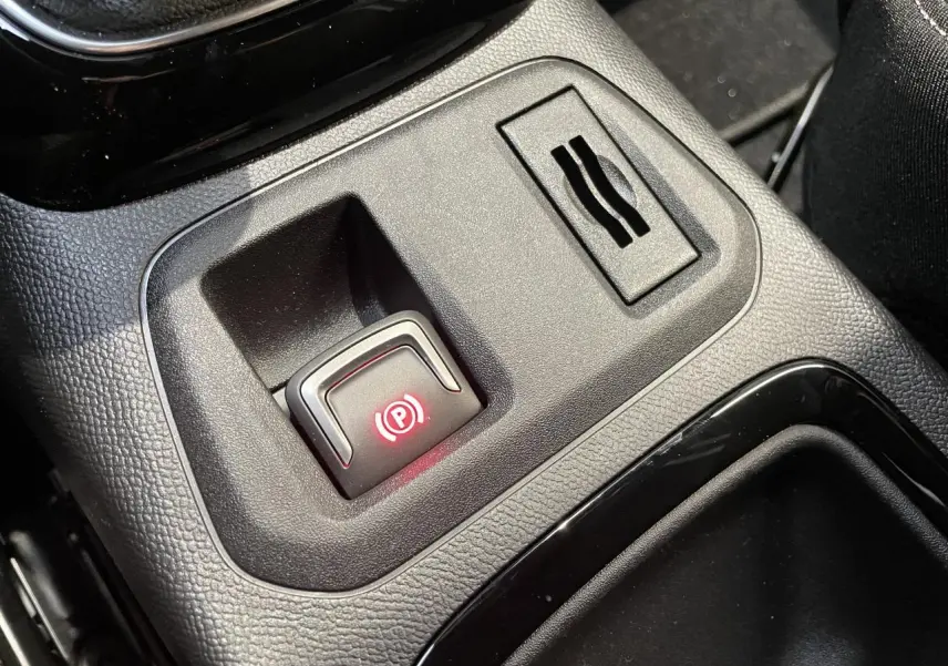 Gros plan sur le frein de parking électrique illuminé en rouge dans la console centrale noire de l'Opel Corsa blanche.