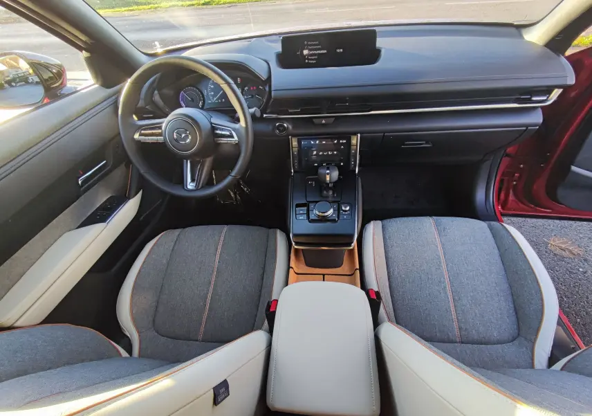Vue intérieure avant du Mazda MX-30 rouge métal 2023, montrant le tableau de bord moderne et les sièges bicolores gris et beige.