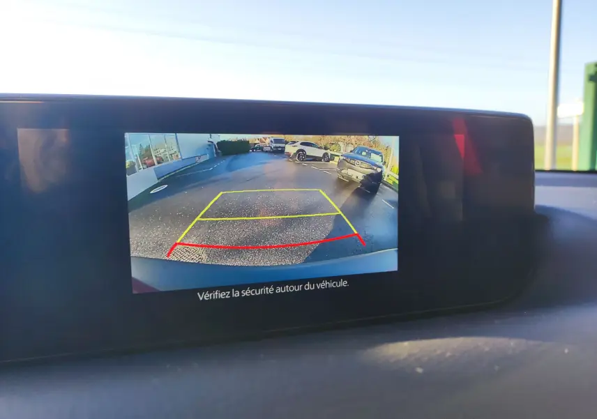 Écran de caméra de recul d'une Mazda MX-30 rouge métal montrant l'arrière et les lignes de guidage au parking.