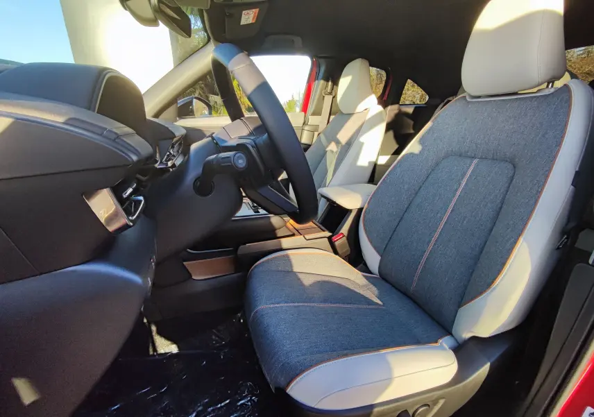 Intérieur avant droit de la Mazda MX-30 rouge métal 2023, sièges bi-matière gris et blanc avec surpiqûres orange.