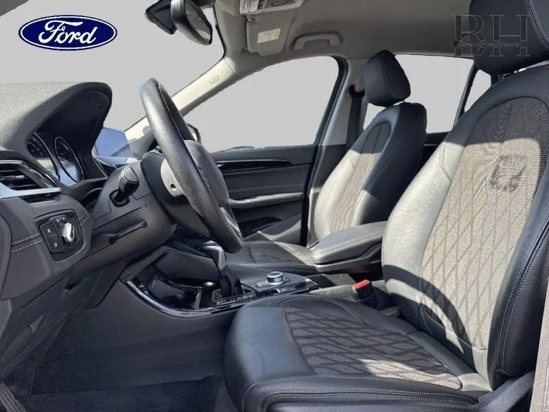 Vue intérieure côté conducteur du BMW X1 xDrive25eA 2021 avec sièges cuir noir et tissu gris à motifs géométriques.