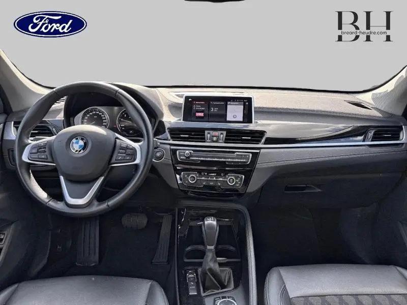 Vue intérieure frontale du tableau de bord et volant cuir multifonction d'une BMW X1 xDrive25eA 2021 en noir.