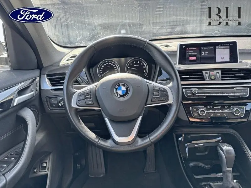 Vue intérieure centrée sur le volant cuir noir et le tableau de bord du BMW X1 xDrive25eA 2021.