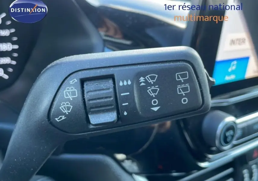 Gros plan sur la commande d’essuie-glace dans l’habitacle d’une Ford Fiesta blanche, avec écran tactile en arrière-plan.
