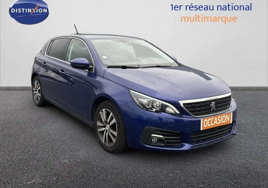 Peugeot 308 bleu Magnetic vue 3/4 avant droit avec calandre chromée et plaque "OCCASION" orange.