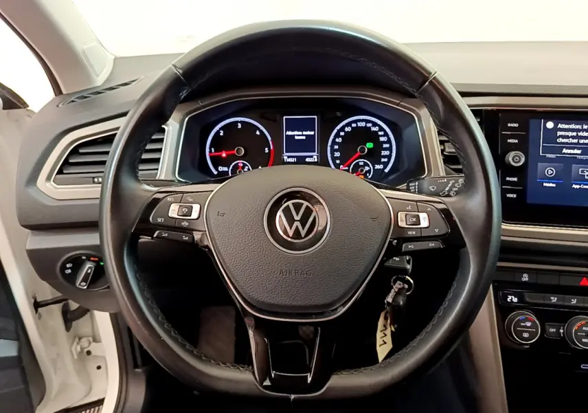 Vue frontale du volant cuir noir et tableau de bord numérique du Volkswagen T-Roc blanc 2021 avec écran tactile central.