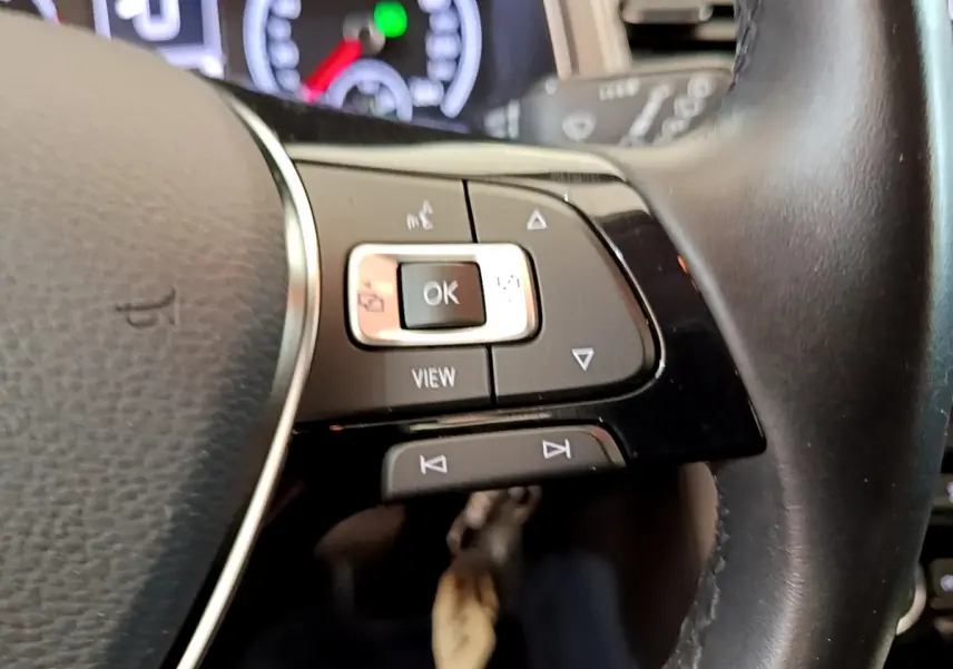 Gros plan sur les commandes multifonctions du volant cuir du Volkswagen T-Roc, avec tableau de bord numérique en arrière-plan.