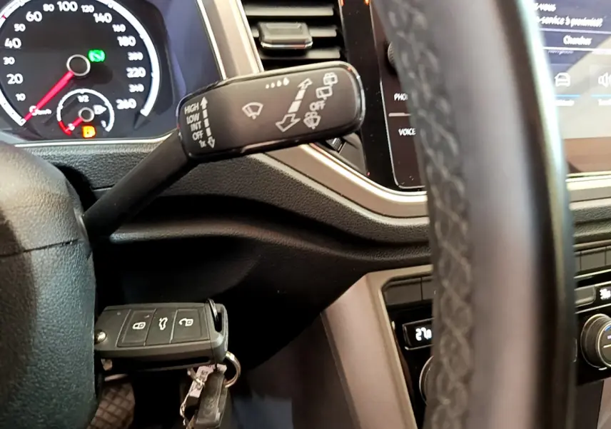 Gros plan sur la manette d’essuie-glace et le tableau de bord du Volkswagen T-Roc blanc, avec clé insérée.