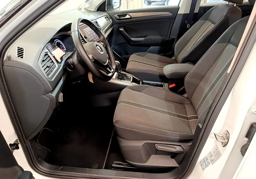 Intérieur avant droit d'un Volkswagen T-Roc blanc 2021, sièges tissu gris et tableau de bord avec écran tactile.