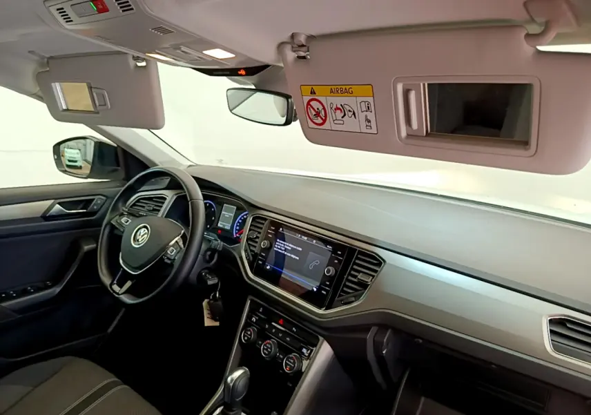 Intérieur du Volkswagen T-Roc blanc 2021 vu côté conducteur, tableau de bord avec écran tactile et volant multifonctions cuir.