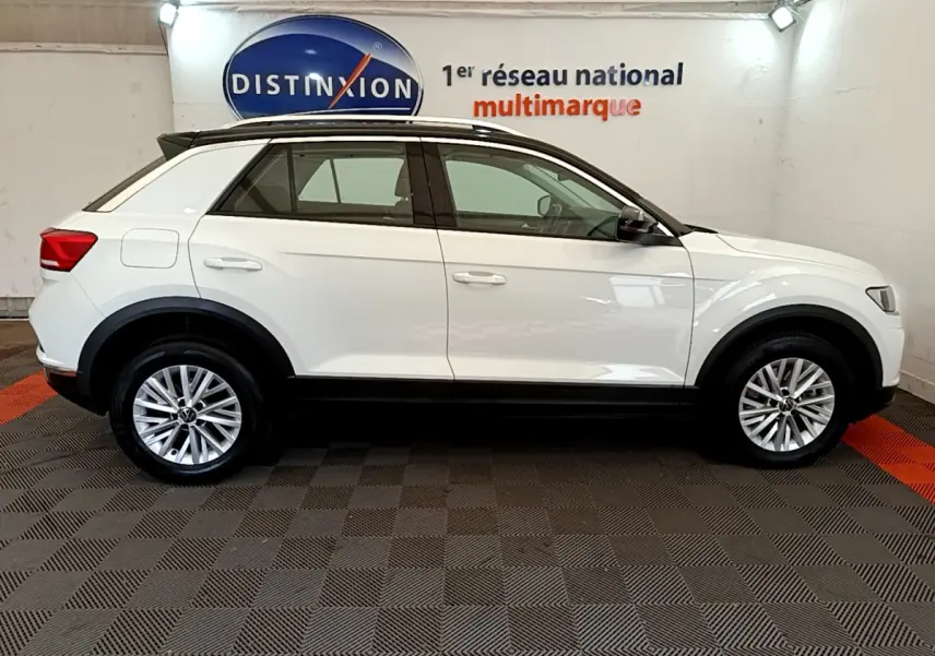 Profil droit d'un Volkswagen T-Roc blanc 2021 avec jantes alliage et toit noir dans un showroom intérieur.