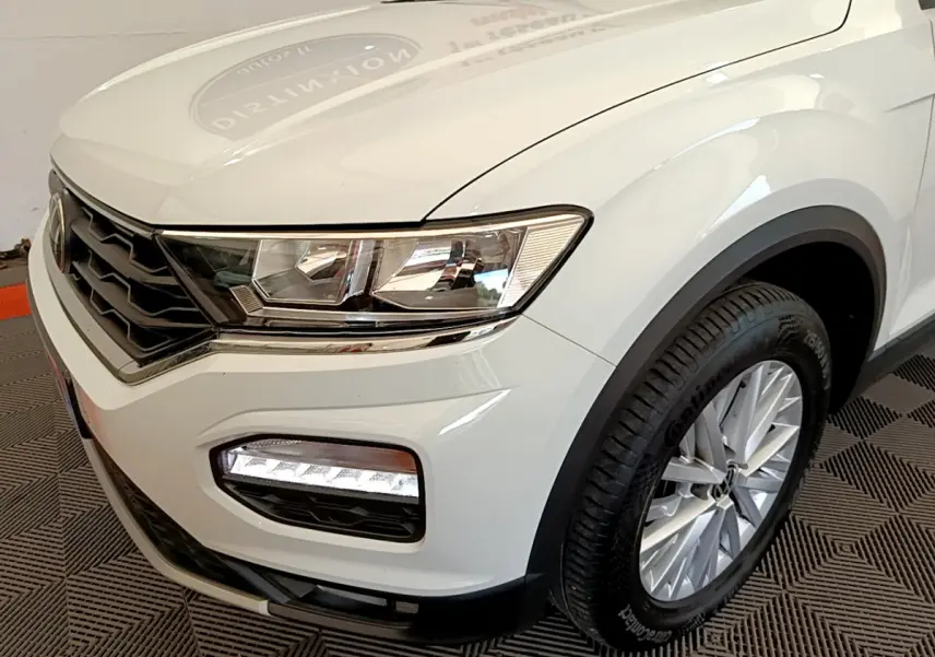 Vue 3/4 avant droit d'un Volkswagen T-Roc blanc mettant en valeur ses phares et jantes alliage.