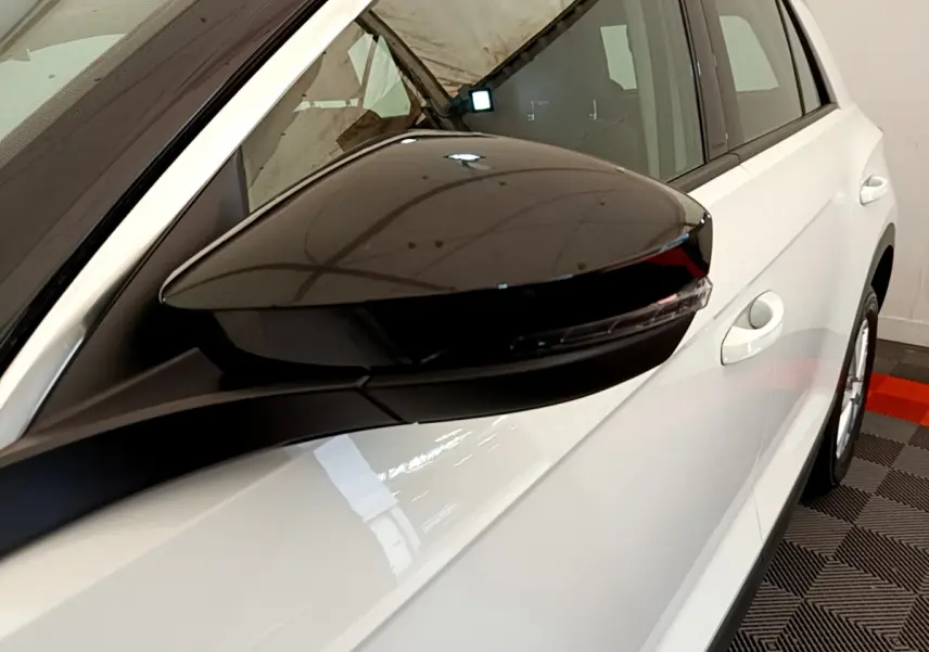 Rétroviseur noir côté conducteur en gros plan sur Volkswagen T-Roc blanc, vue latérale droite du véhicule.